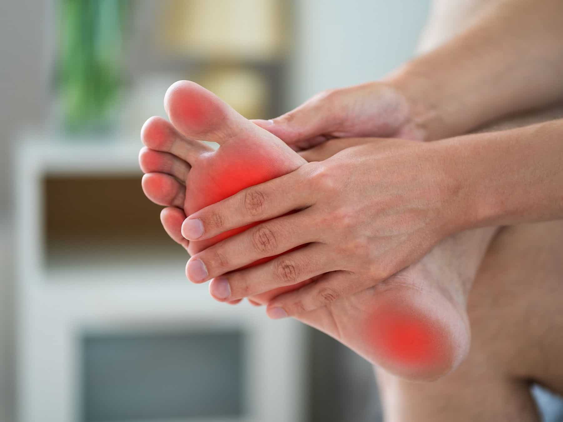 Person holding their foot with a red spot on it