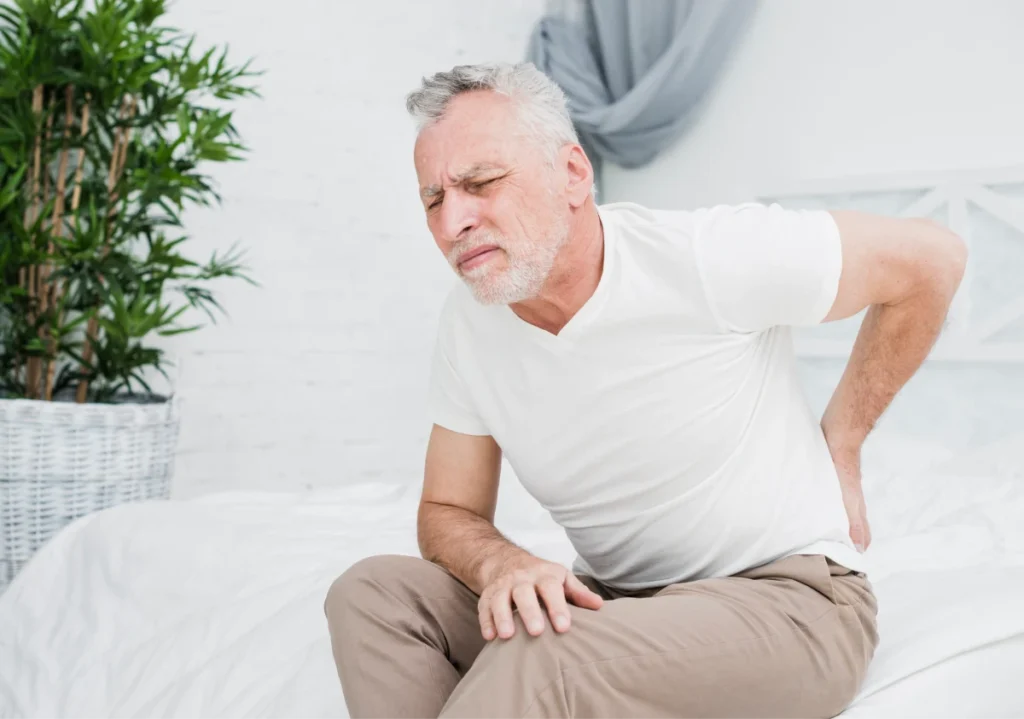 What Is Rheumatology? 3 Older man sitting on bed, holding his lower back in pain.