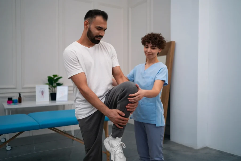 A physical therapist assisting a man in lifting his leg during a rehabilitation exercise in a clinical setting.